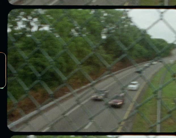 A fenced footbridge over a busy freeway on a cloudy day