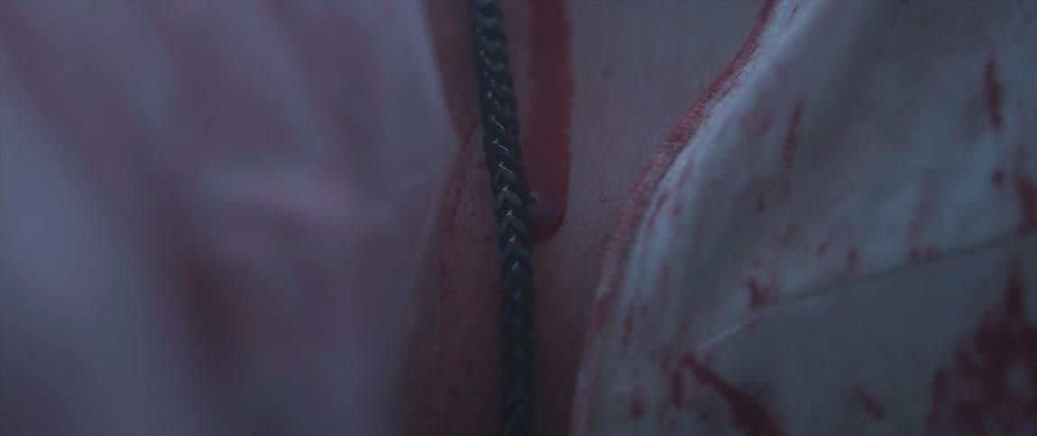 Blood slowly drips down a womans chest past a chain and blood stained clothing