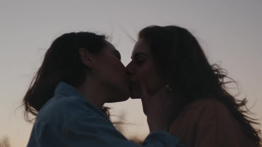 Two women kiss at sunset on a rooftop
