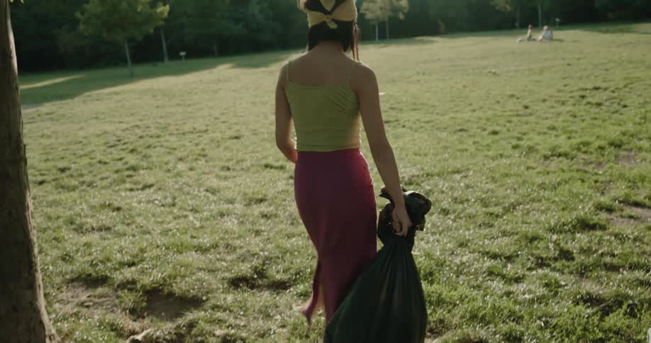 Friends put trash in bag before carrying it with them through park on sunny day