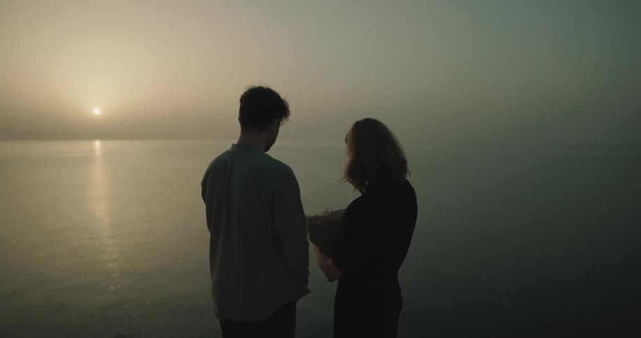 Woman throwing ashes into the sea on a foggy morning as a man watches