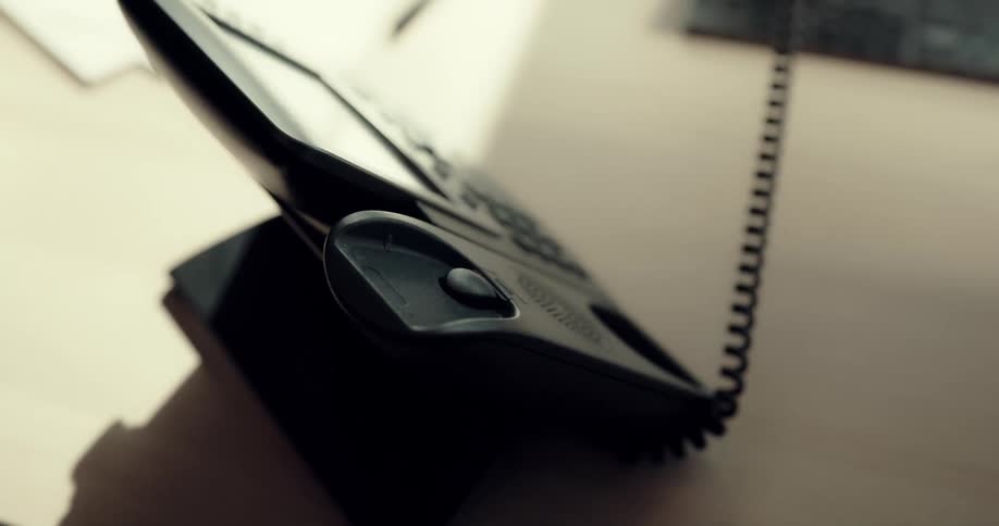 A person answers a desk phone before returning it to its stand