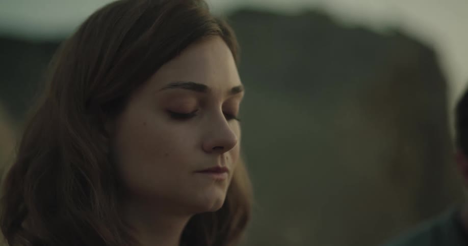 Woman stands with eyes closed next to man with mountain in the background