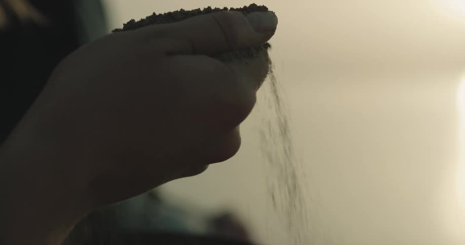 A person picks up ashes from an urn to disperse them over the ocean at sunset