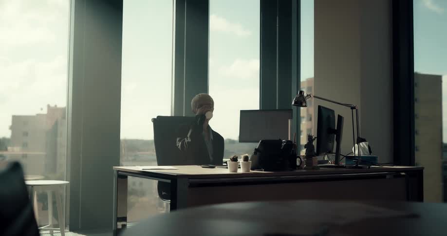 Businesswoman with short hair blazer jacket pants and shirt sits in chair and drinks cup of coffee in the office