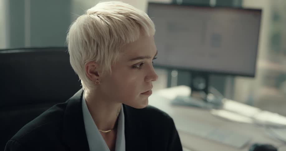 A woman drinking from a disposable coffee cup sits down at a desk in an office and answers the phone
