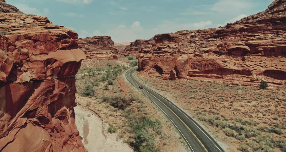 A red truck travels on highway road through desert canyons under a cloudy sky