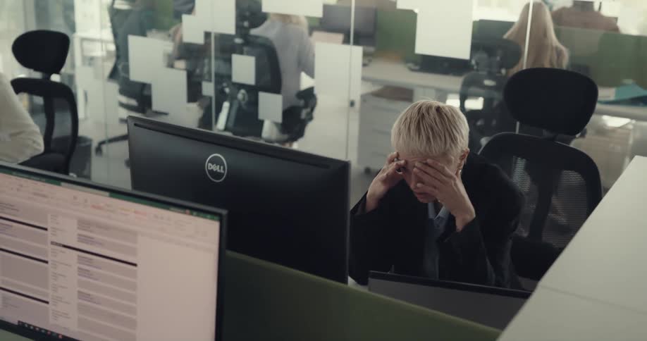 A man gets up from leaning against a desk points to his watch giving a frustrated and sad employee a deadline