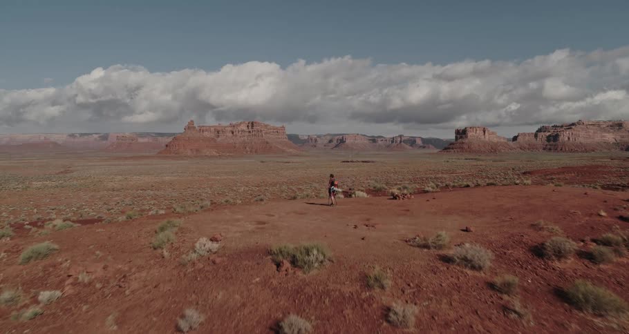 Aerial view of a man standing on hill in the desert overlooking the badlands under a cloudy sky