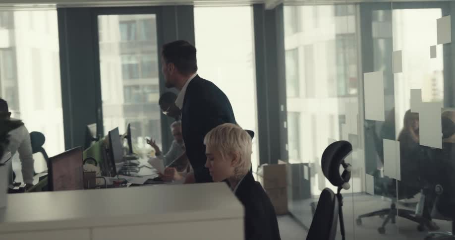 A man in an office stands next to a woman and yells at her and turns to other employees and throws a stack of papers in the air and storms off