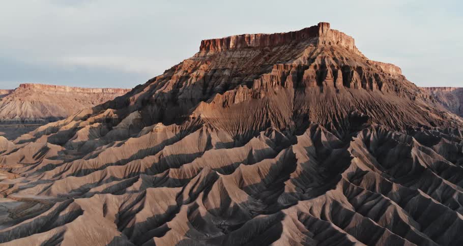 A mesa stands tall in the desert as the sun shines brightly upon it