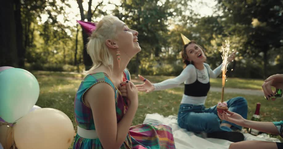 A group of women party horns while sitting together on a blanket in a park