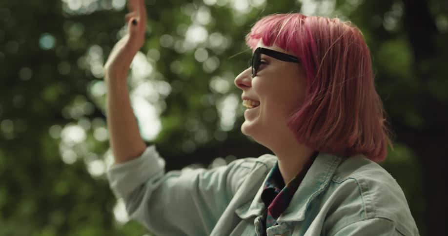 A woman smiles and smokes outside as she waves at someone