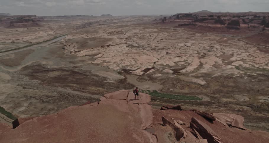 A man stands on a cliff overlooking a river in a vast canyon