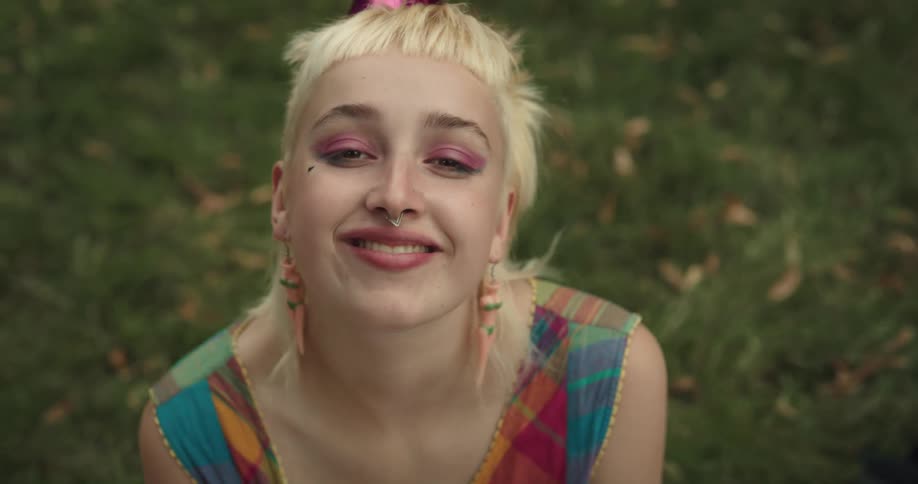 Blonde woman wearing party hat sits on ground smiling and blowing a kiss