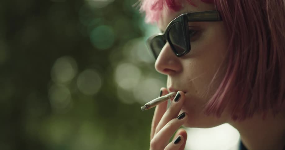 A woman takes a drag of her joint then turns her head and exhales smoke