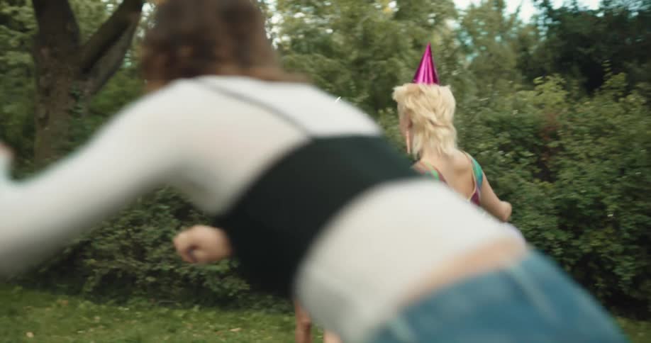 Group of friends wearing party hats celebrate with balloons and soap bubbles in the park