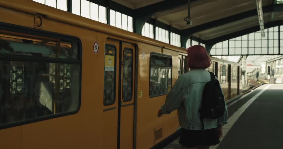 A teenage girl with a backpack on her shoulder is waiting for a train and gets on when it stops