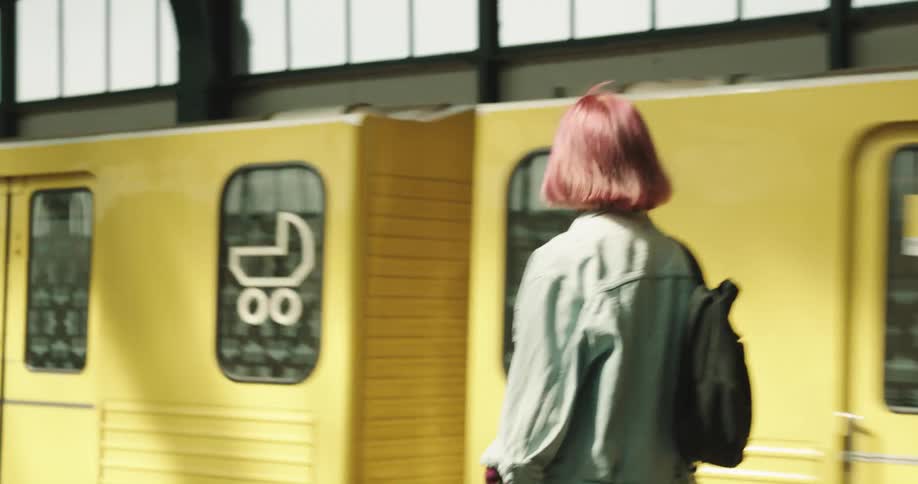 A woman walks down a train platform then boards a train as it stops