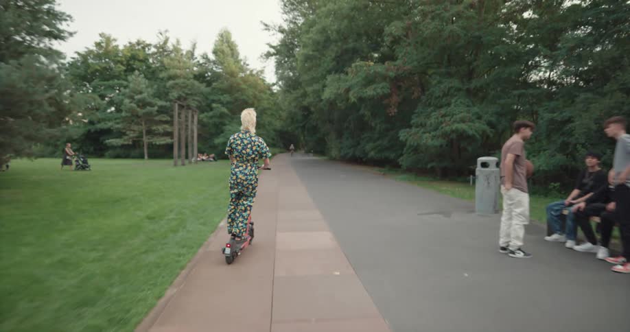 A person rides past pedestrians in the park on a scooter