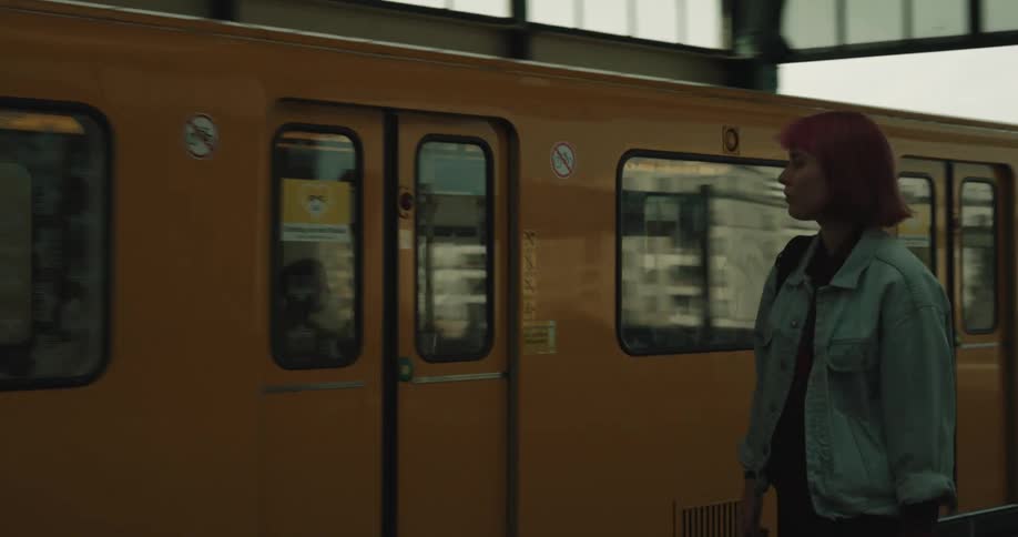 A teenage girl is sitting at a rapid station waiting for her train and she gets up and puts her backpack on her shoulder and gets on the train when it stops