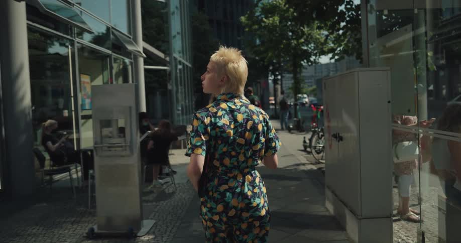 A young woman drinks from a disposable coffee cup while walking through a metropolis during the day