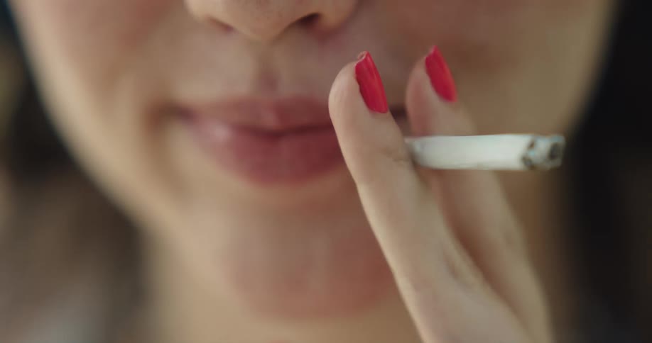 Close up of the mouth of a woman smoking a cigarette and blowing smoke
