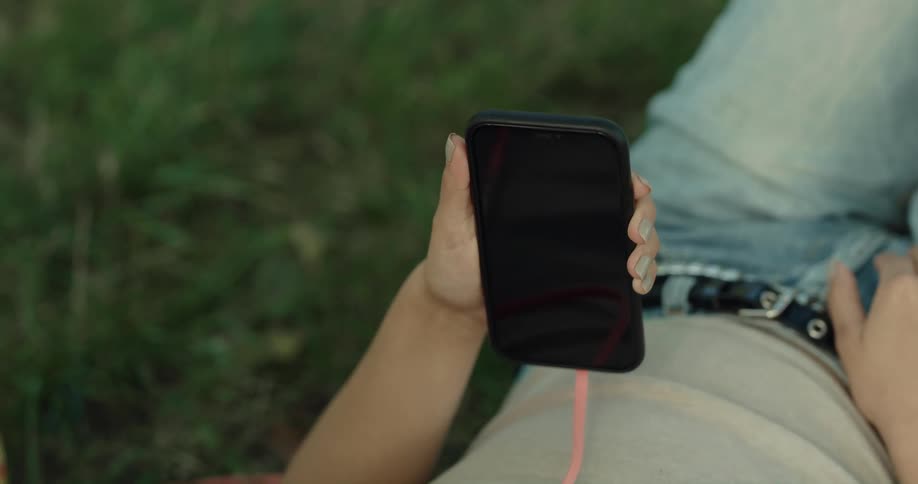 A woman is laying in the grass holding and scrolling on a cell phone