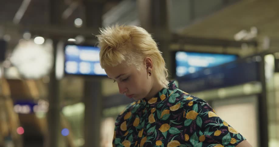 A young woman uses her smartphone while waiting for a train on a subway platform