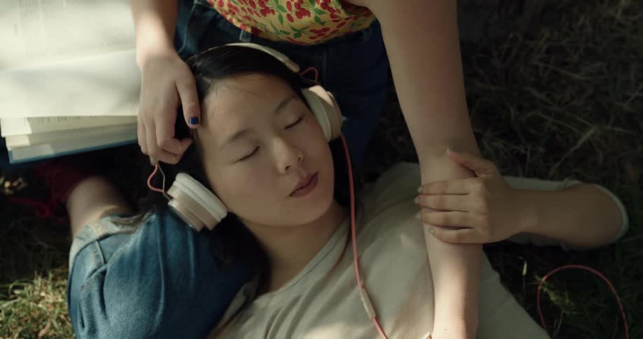A woman resting her head in the lap of another woman smiles while her hair is stroked