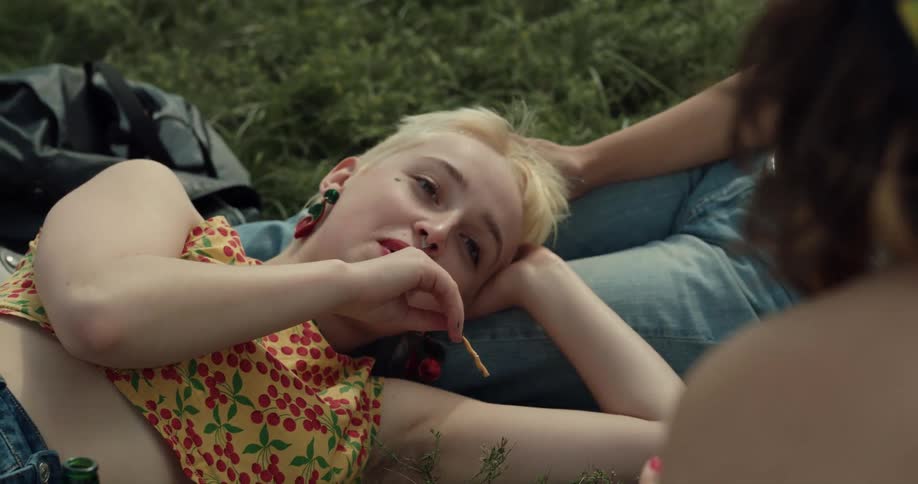 Female friends recline on grass one feeding another pocky sticks