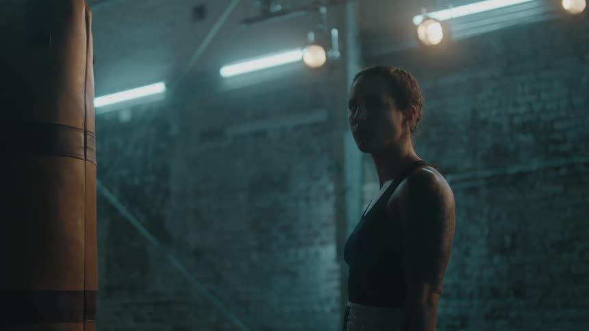 A woman is in a poorly lit room boxing