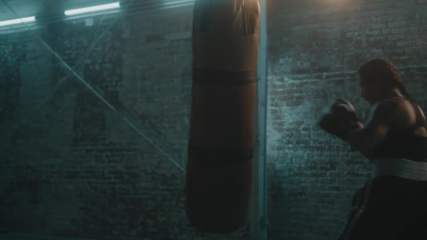 A female boxer strikes a punching bag in a dimly lit room