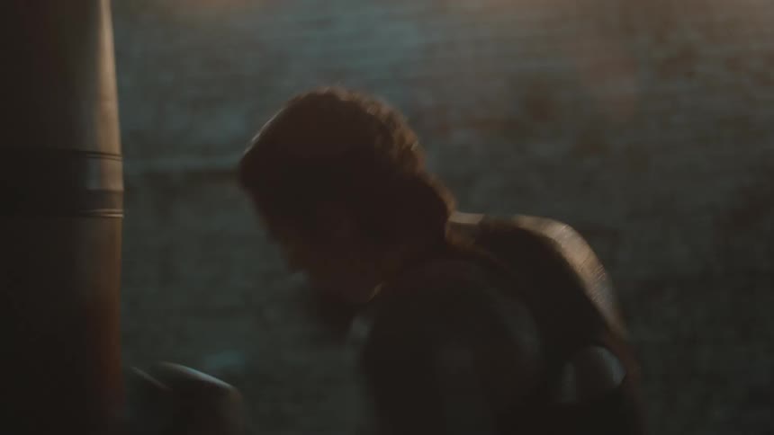 A female boxer strikes a punching bag in a dimly lit room