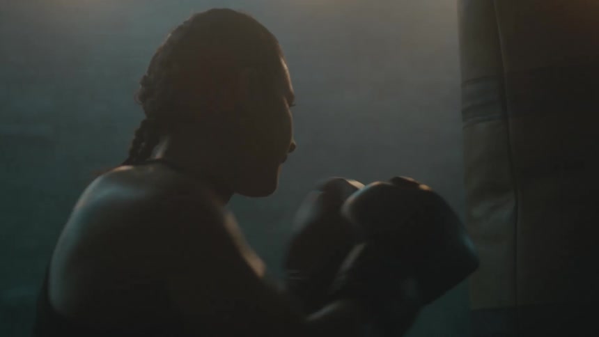 A female boxer trains by striking a punching bag in a dimly lit room