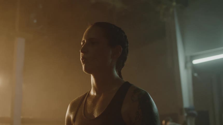 Female boxer with braids tattoo and sports bra stands in boxing ring