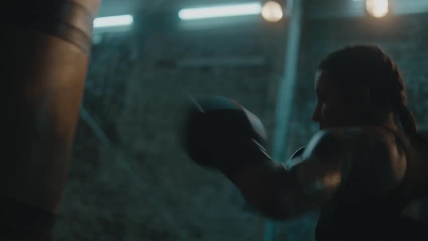 Female boxer with braids sports bra boxing trunks hits punching bag in the gym