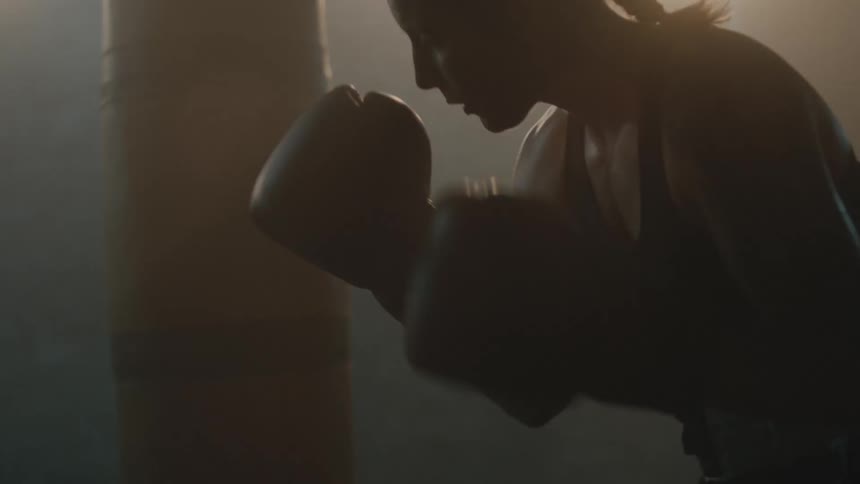 A woman is boxing indoors while the sun is setting