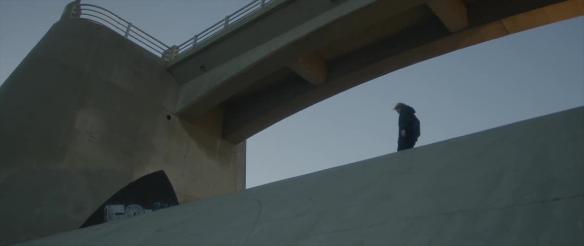 Person walks across top of sloping concrete slab under bridge