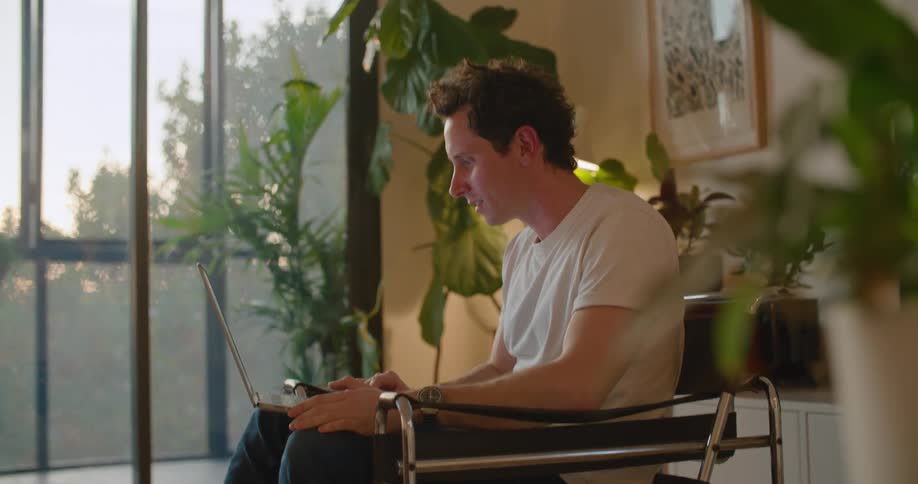 A man is sitting indoors and video chatting on his laptop