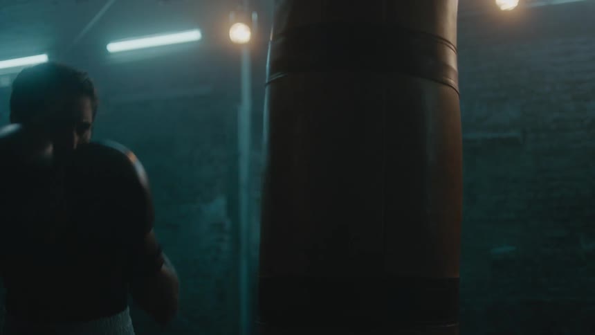 Female boxer trains with heavy bag in dim gym