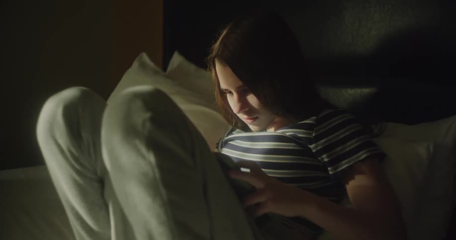 A woman sitting in bed with her knees up playing on a tablet