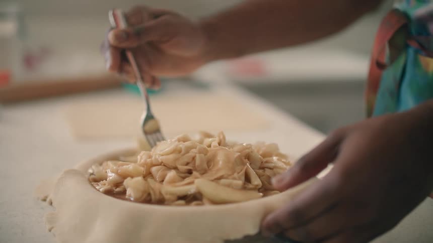 A person is stirring a bowl of noodles in a kitchen