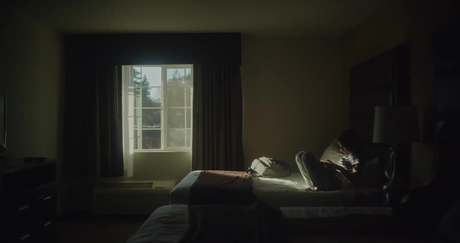 A girl sits on a bed in a hotel room and uses a tablet