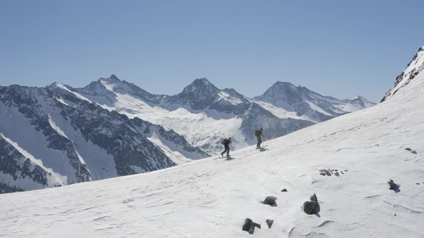 A pair of mountaineers climb a snowy slope on a mountain during the day