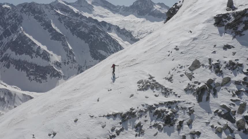 A mountaineer climbs a snowy mountain slope during the day