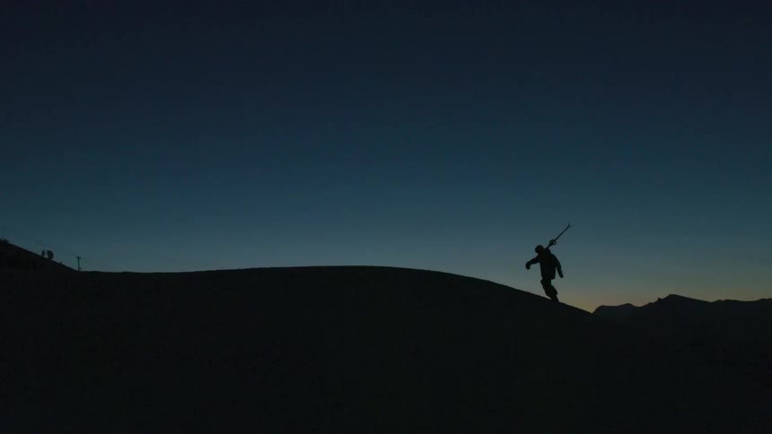 Silhouette of a man carrying skis over a mountain at evening