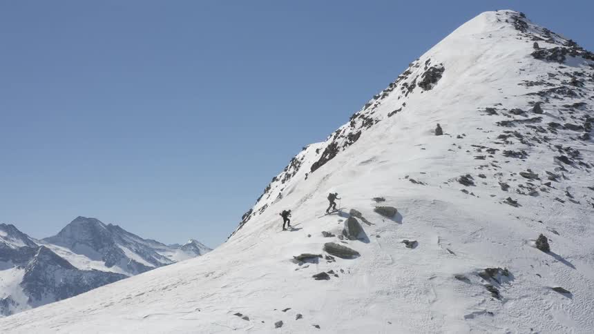 Two people are climbing a snow covered mountain under a clear blue sky