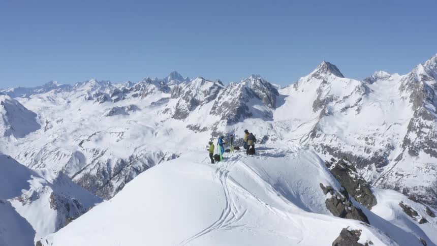 A group of people is at the top of a mountain in a snowy mountain range