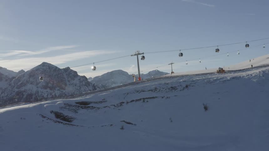 People ski down a snow covered mountain under a moving gondola